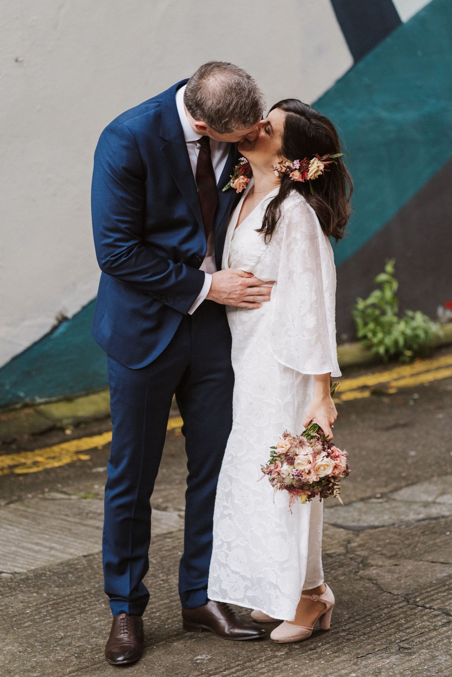 A couple in wedding attire sharing an intimate kiss, with the bride in white lace and groom in navy suit.