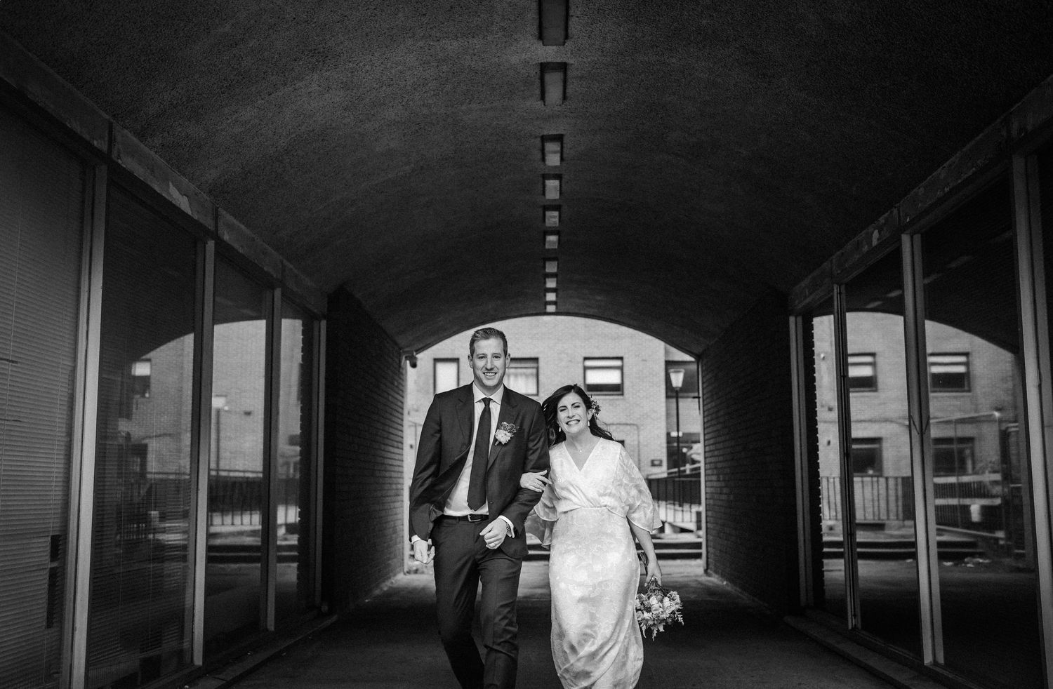 A couple poses under an arched tunnel walkway in black and white wedding photography.