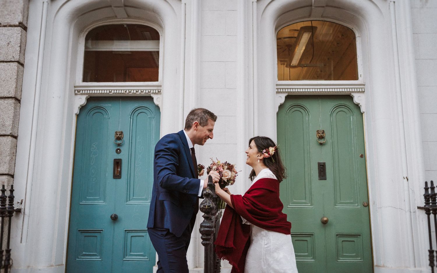 Romantic wedding couple poses in front of historic turquoise doors at elegant venue during winter photo session.