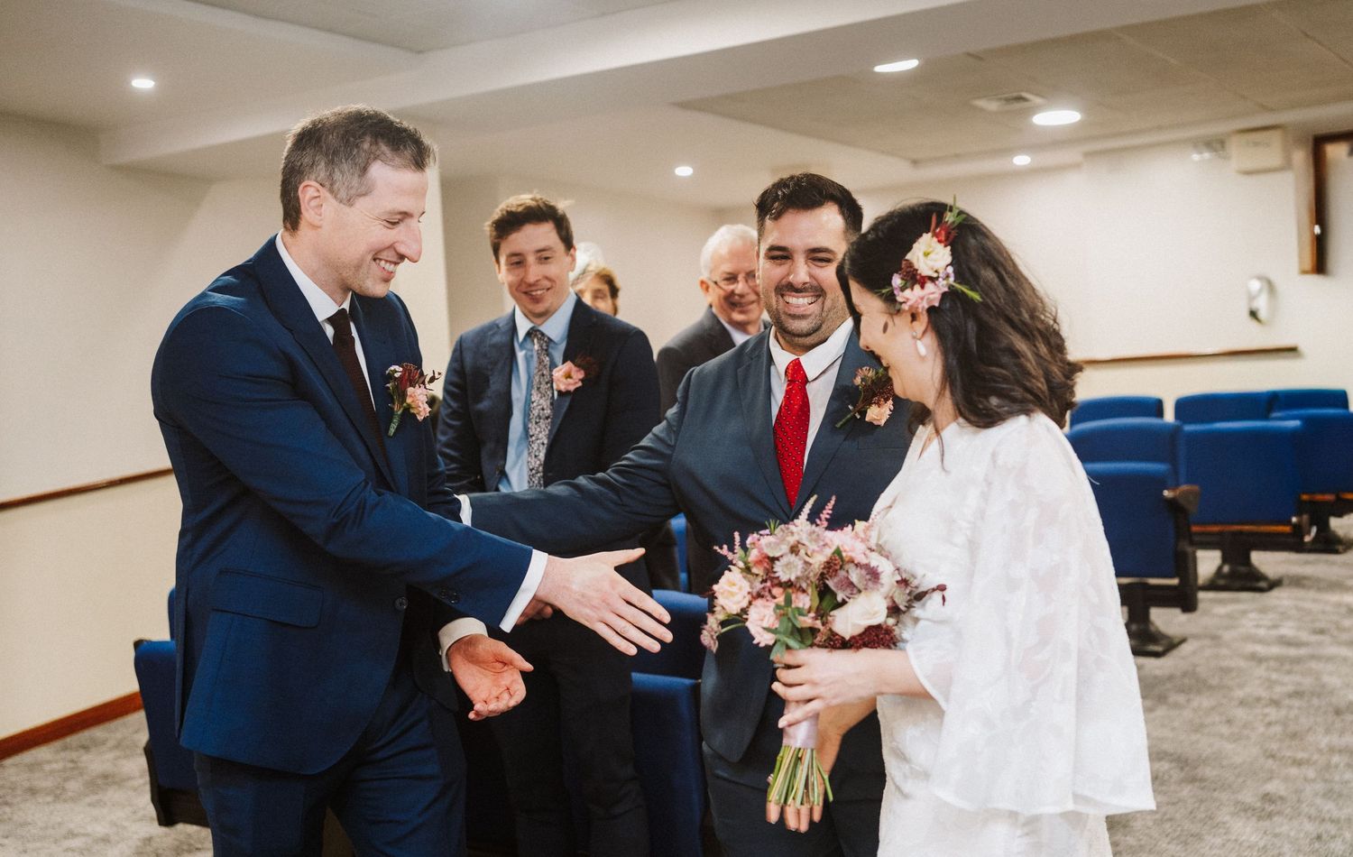 A sequence of five photos showing a wedding ceremony and celebration in an indoor venue with blue seating.