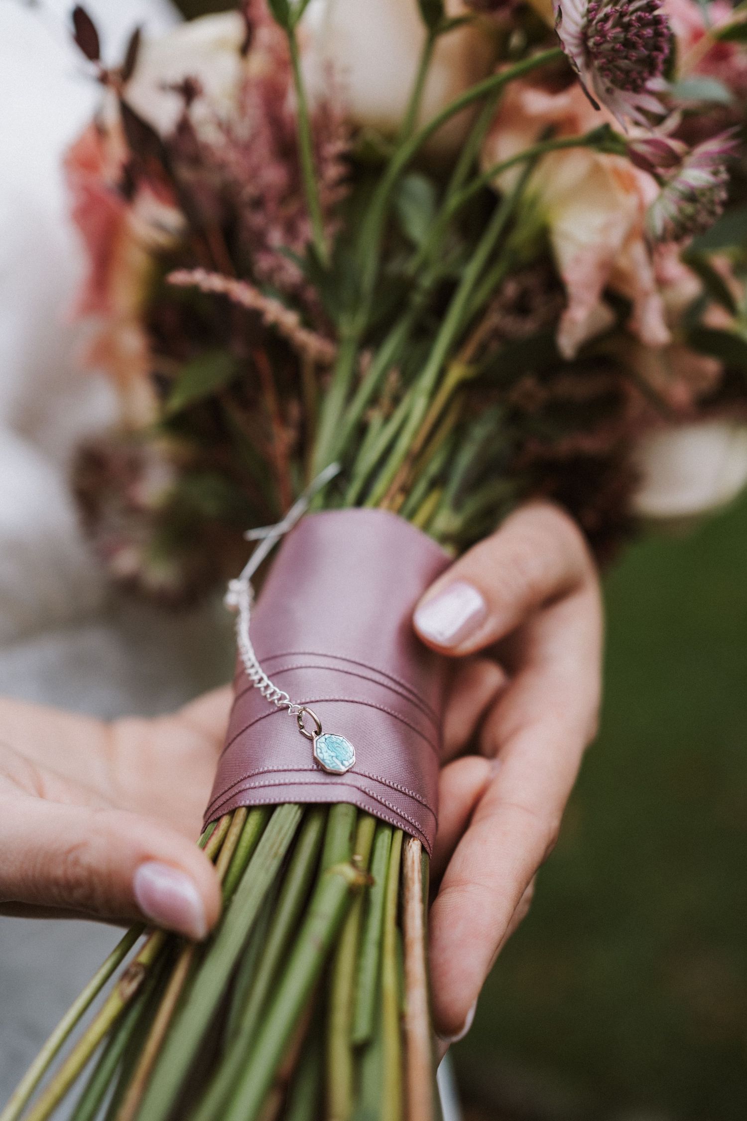 Hands hold a bouquet wrapped in pink leather with a delicate crystal charm detail.