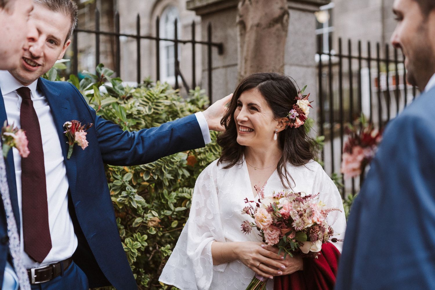 Wedding guests laugh and smile during an outdoor garden reception near stone architecture.