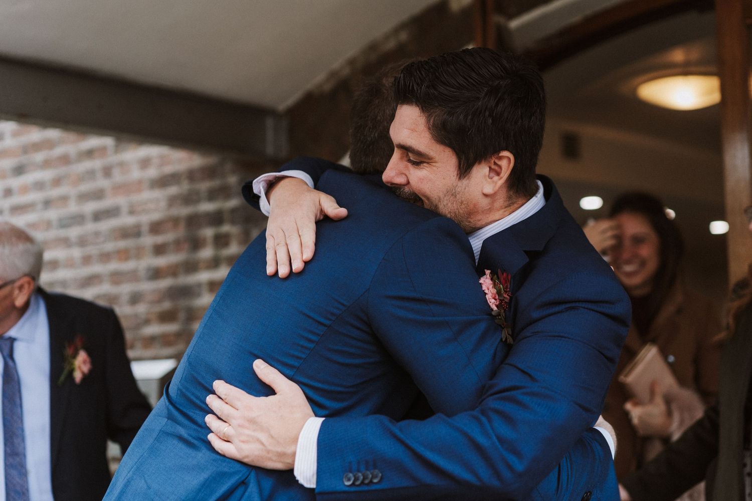 People in navy blue suits embrace during what appears to be a formal celebration or gathering.