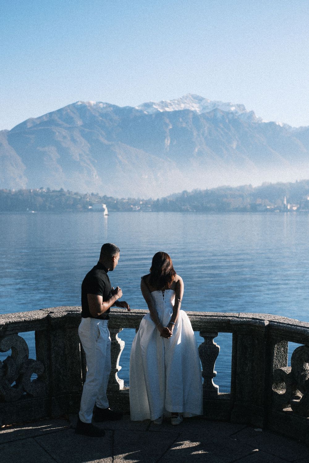 People admiring scenic mountain views across Lake Como from a stone terrace in Italy.