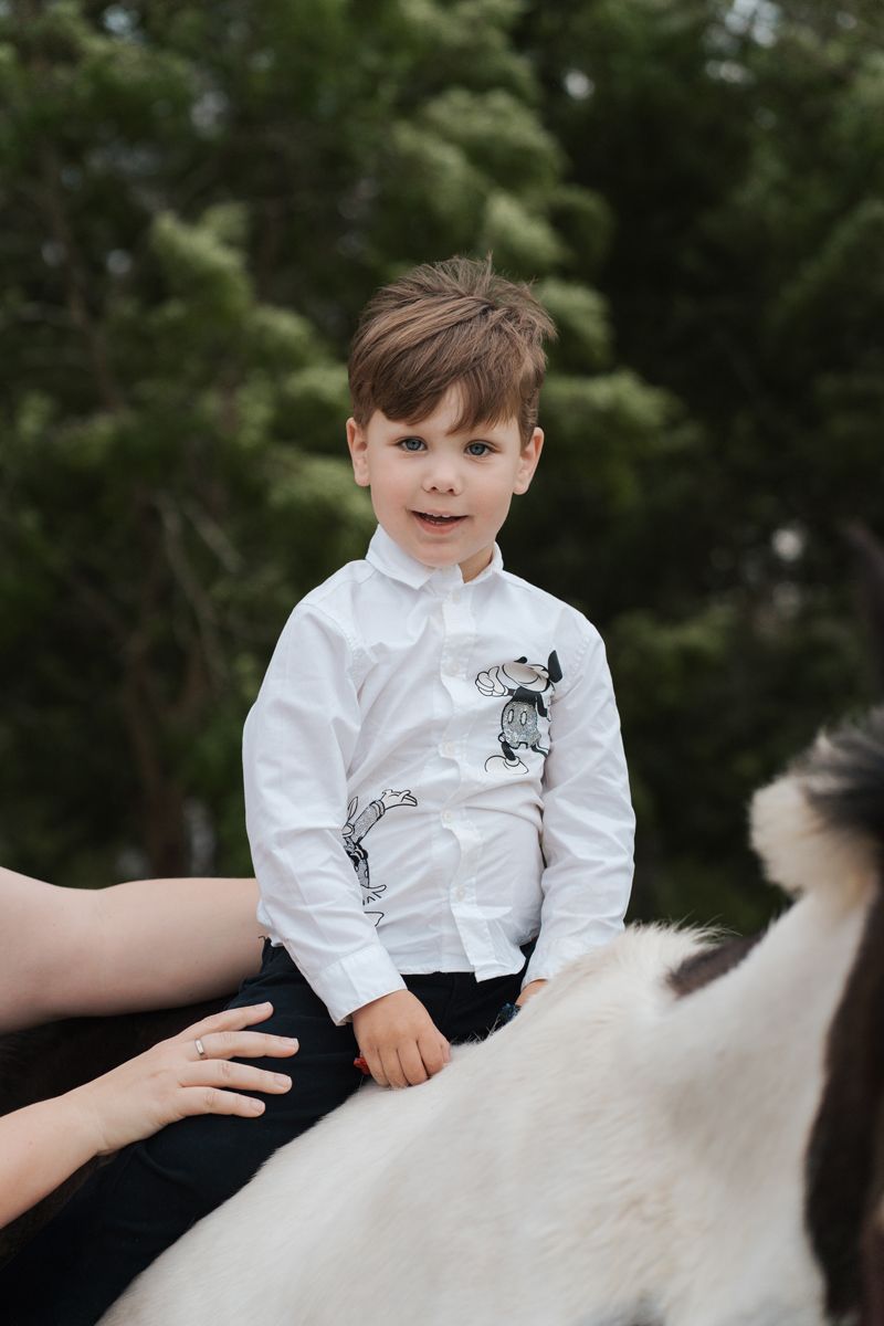 A young child in formal white shirt and black pants sits on a white horse in an outdoor setting during a horse photoshoot in sydney