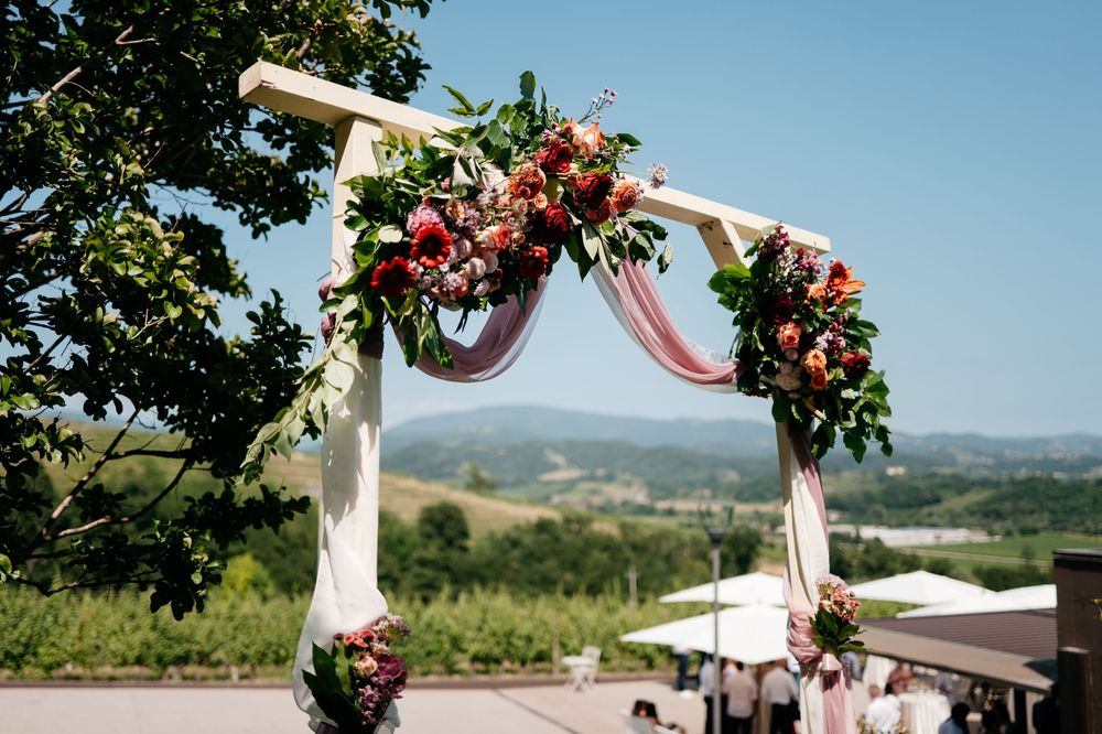 Outdoor wedding ceremony arch decorated with pink and red flowers against a mountain landscape.