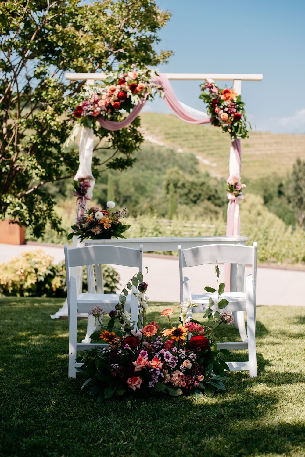 White wooden chairs and floral arrangements set up for an outdoor garden wedding ceremony.