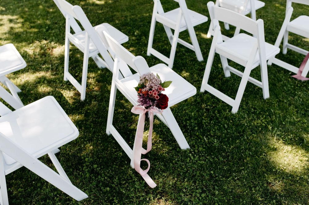 Row of white folding chairs set up on green grass for an outdoor ceremony.