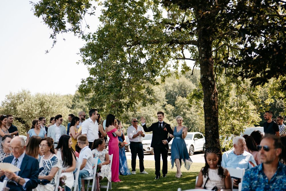 Wedding guests mingling outdoors under tree canopy during a daytime celebration.