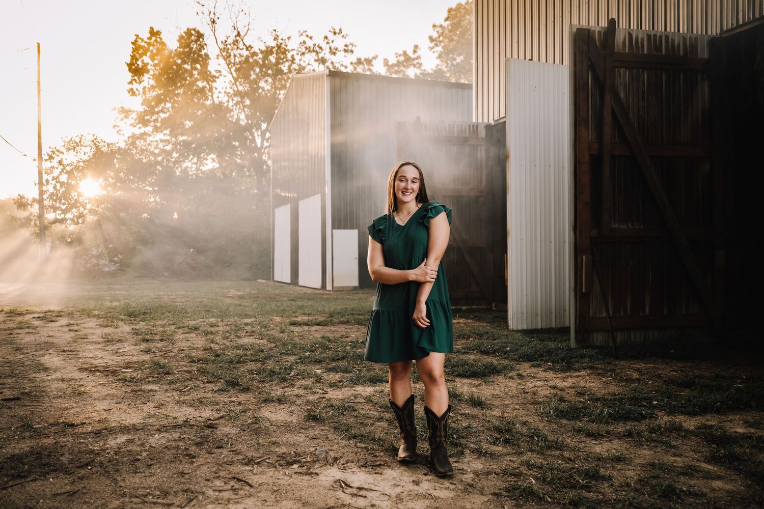 A figure stands in front of a rustic barn during golden hour with sunlight creating a dreamy, misty atmosphere.