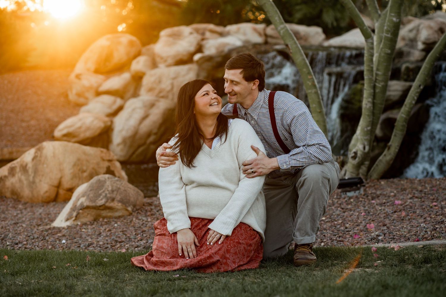 Couple shares a joyful moment sitting together near a waterfall at golden sunset.