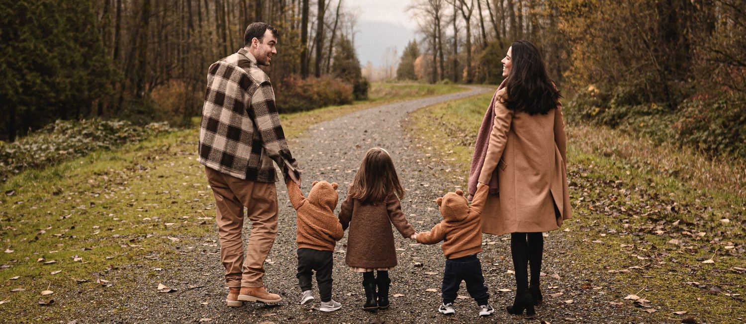 Family of four walking hand in hand on a path surrounded by autumn trees.