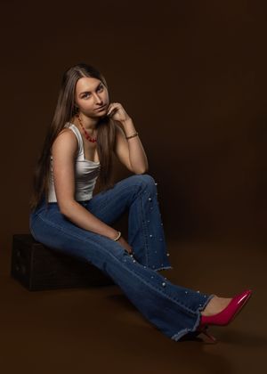 A model in jeans and white tank top poses in multiple reclining positions against a dark background with pink heels.