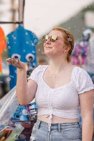 A person in a white crop top and jeans blows bubbles outdoors on a sunny day.
