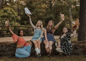 Group of friends sitting together on fallen tree trunk in autumn forest during golden hour sunset.