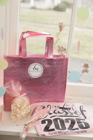 Pink party favor bags with decorative tags sit in a row on a windowsill with soft natural lighting.