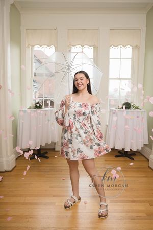 Young girl in a floral dress twirls and dances in a bright room with pink flower petals falling around her.