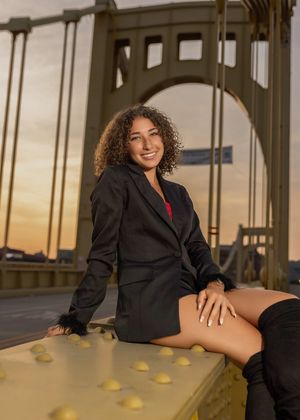 A person in a black blazer poses on a wooden floor with yellow cones visible in the background during sunset.