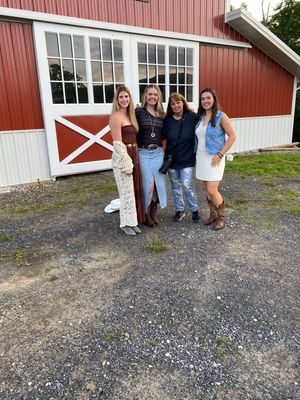People standing in front of a red barn with white trim on a gravel driveway in a casual outdoor setting.