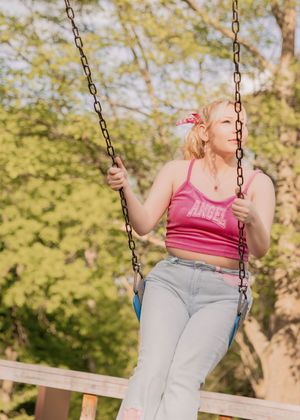 Person in pink tank top and jeans enjoys swinging at a park on a sunny spring day.