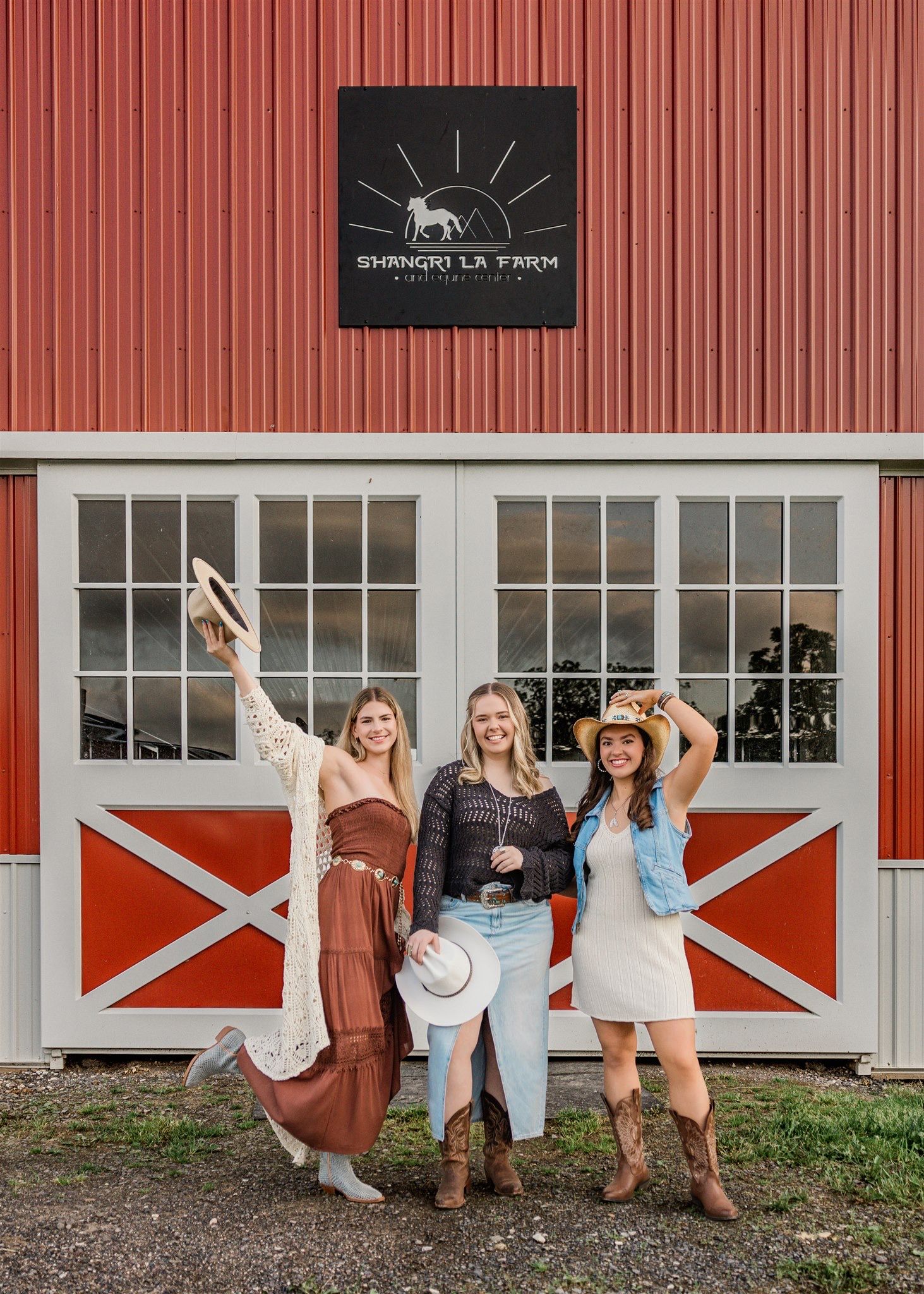 Group posing in casual summer outfits against a red barn-style building with white trim and windows.