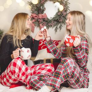 People in matching red plaid holiday pajamas relaxing together with hot cocoa and festive Christmas decor.
