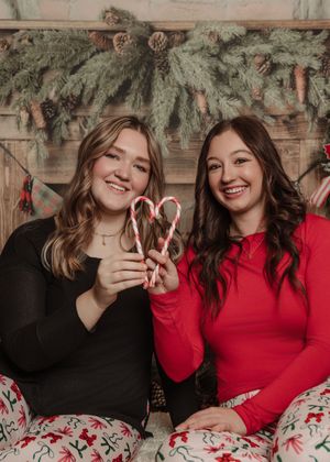 Two people in festive holiday attire sharing a moment under evergreen decorations and Christmas ornaments.