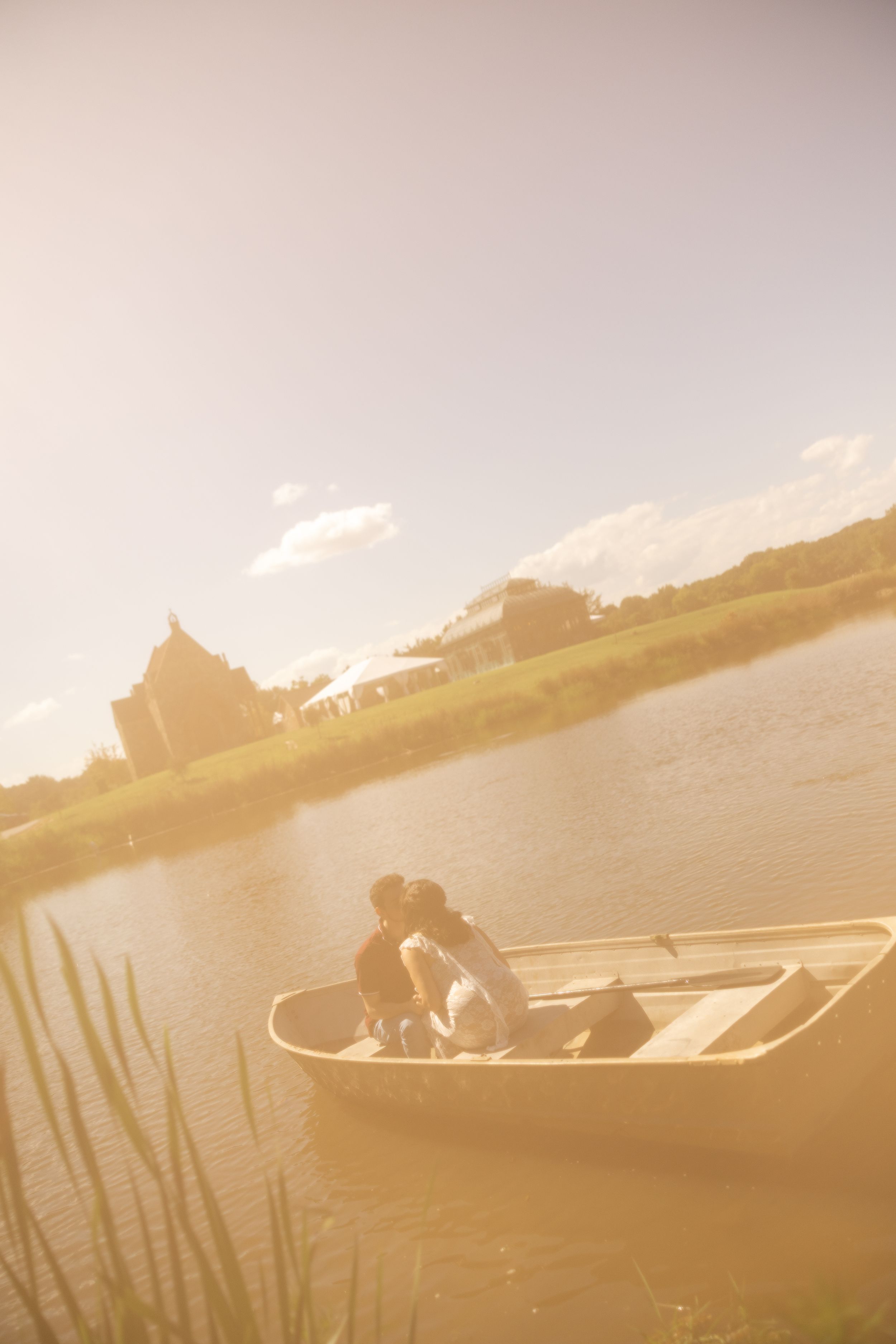 Couple sharing a romantic kiss in a rowboat on a serene lake at golden hour with a castle in the background.