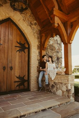 Couple sharing a romantic moment at a rustic stone chapel entrance with wooden arched doors and timber accents.