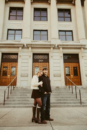Couple posing on steps of a neoclassical building at 301, woman leaning on partner's shoulder.