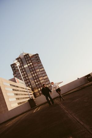Couple playfully running toward each other on a rooftop parking deck with a city high-rise in the background.