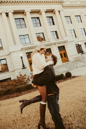 Couple laughing as man lifts woman in front of a classic stone courthouse building.