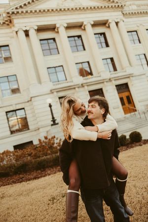 Woman giving her partner a piggyback ride while smiling in front of a neoclassical building.