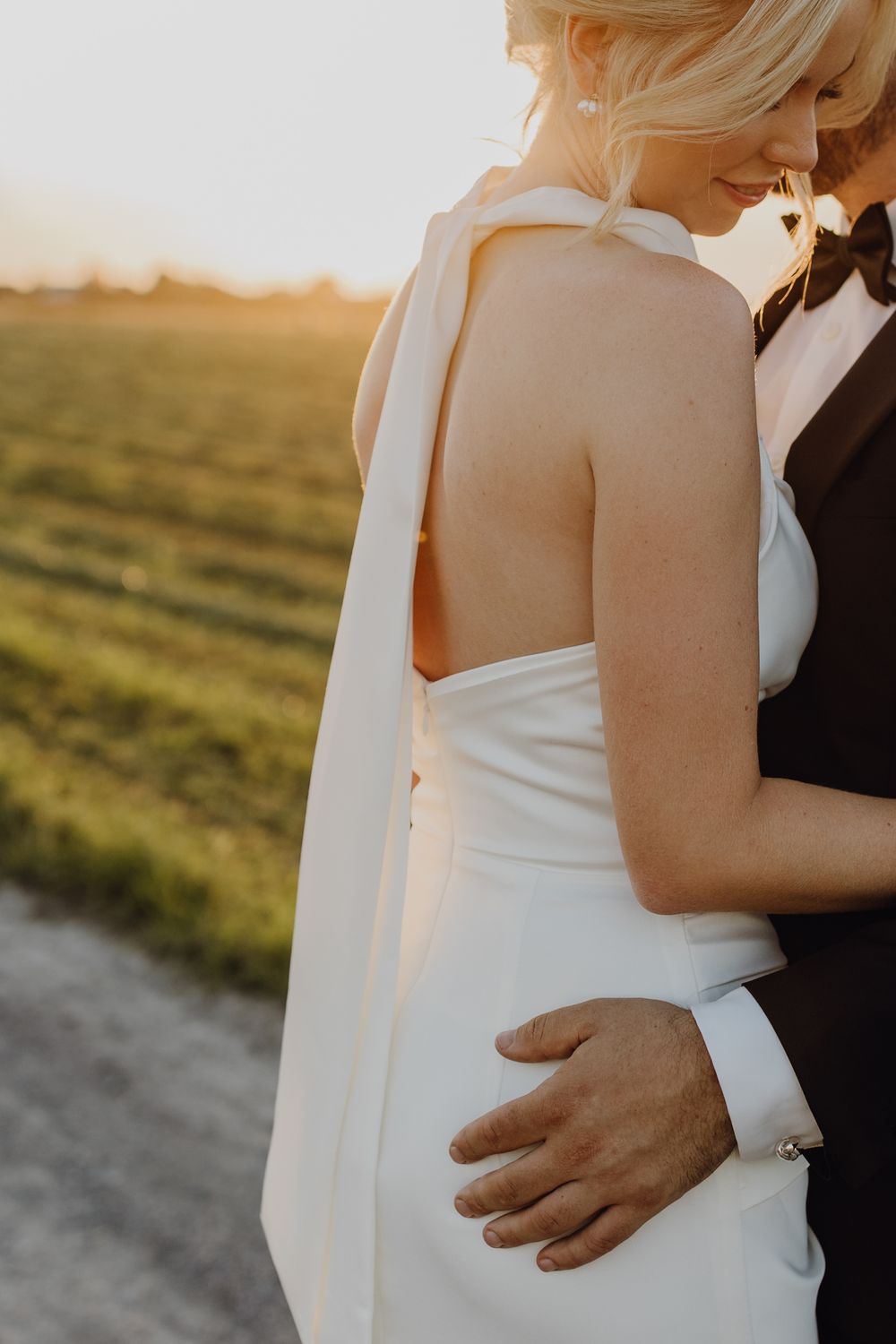 Paarshooting am Hochzeitstag bei Sonnenuntergang, der Fokus liegt auf den eleganten Verschluss des Brautkleid, das im Nacken geschlossen ist