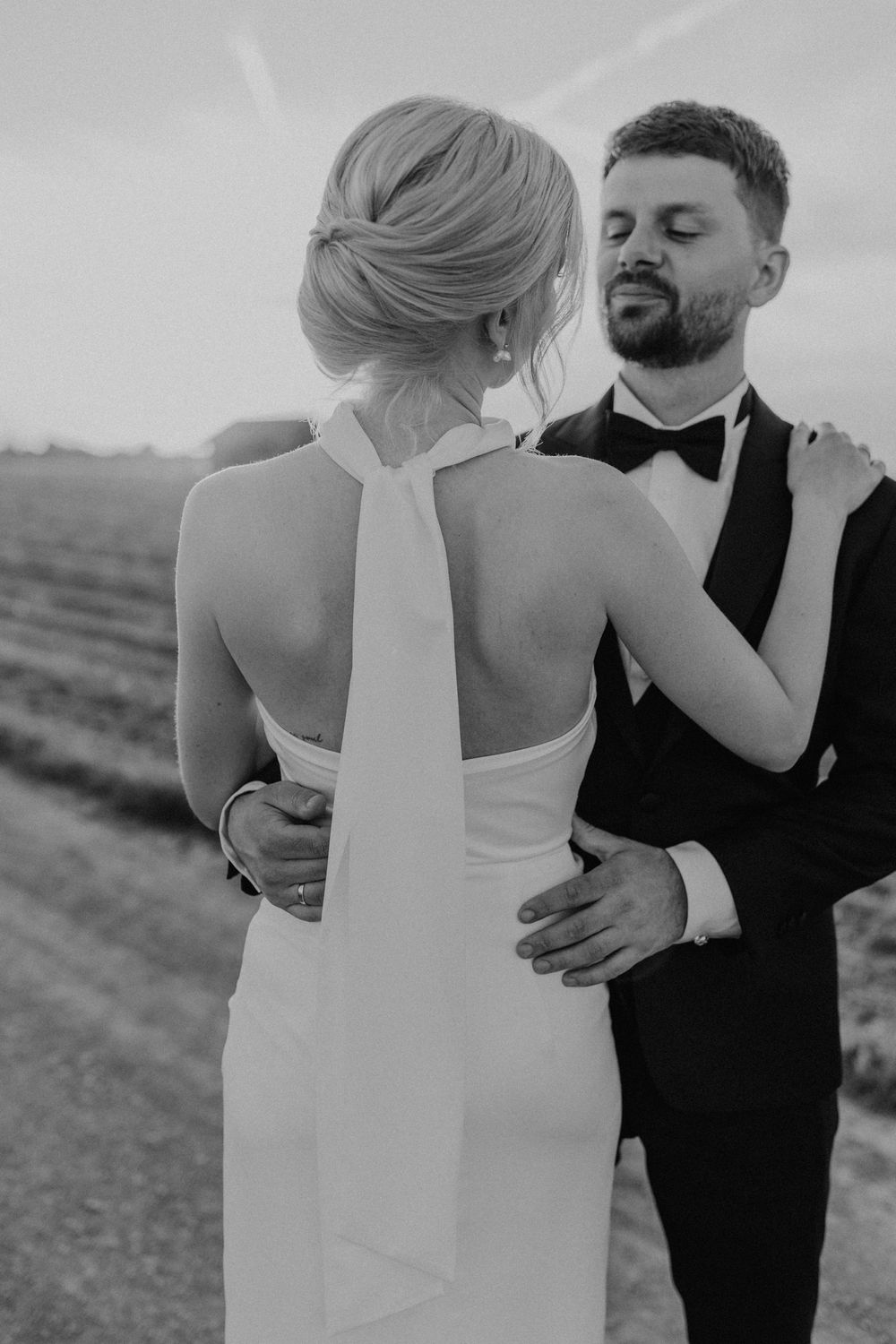 Paarshooting am Hochzeitstag bei Sonnenuntergang, das Brautpaar steht sich gegenüber, man sieht das elegante und schlichte Brautkleid.
