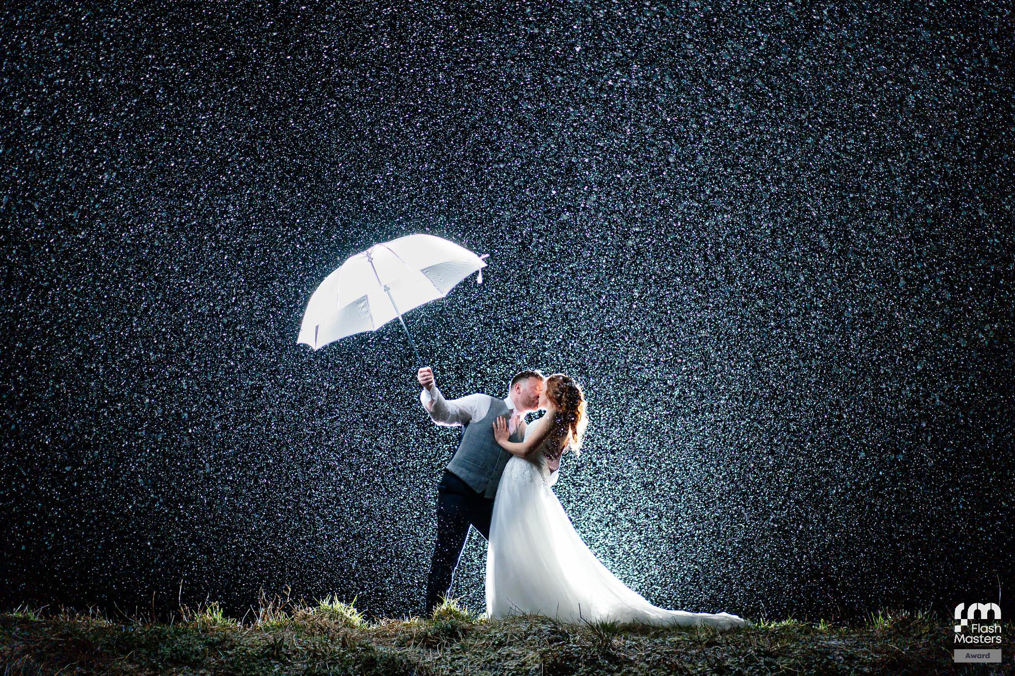 Dramatic nighttime wedding photography with white umbrellas and flowing dress in the rain.