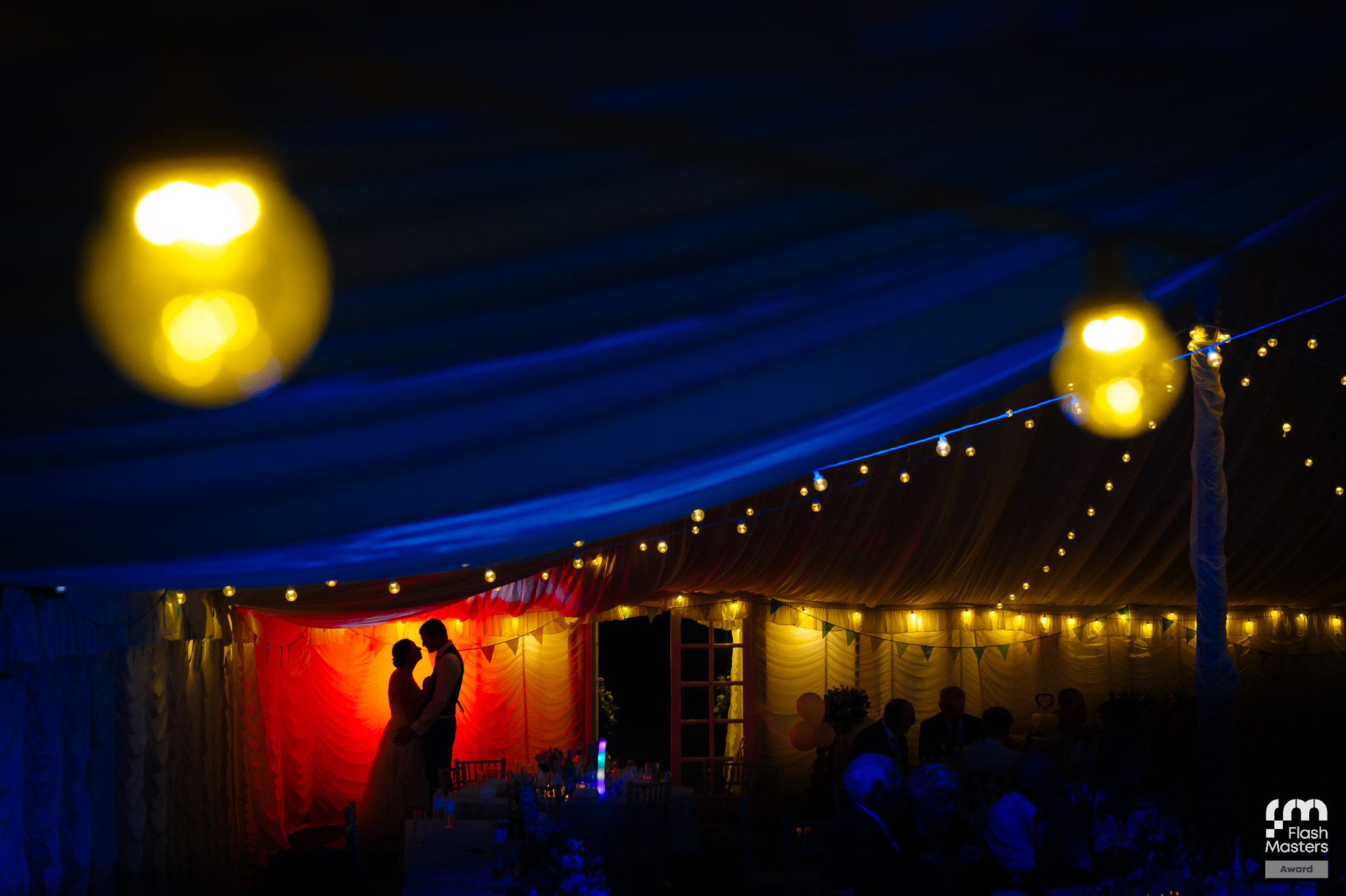 Outdoor evening event space with glowing lanterns and string lights against a deep blue sky.