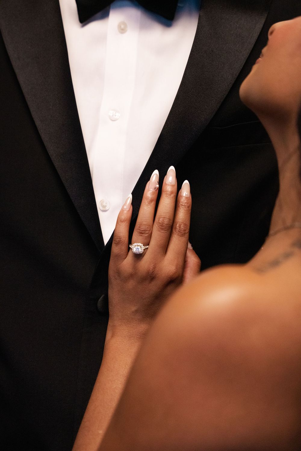 Close-up shot of hands wearing wedding rings against formal black and white attire.