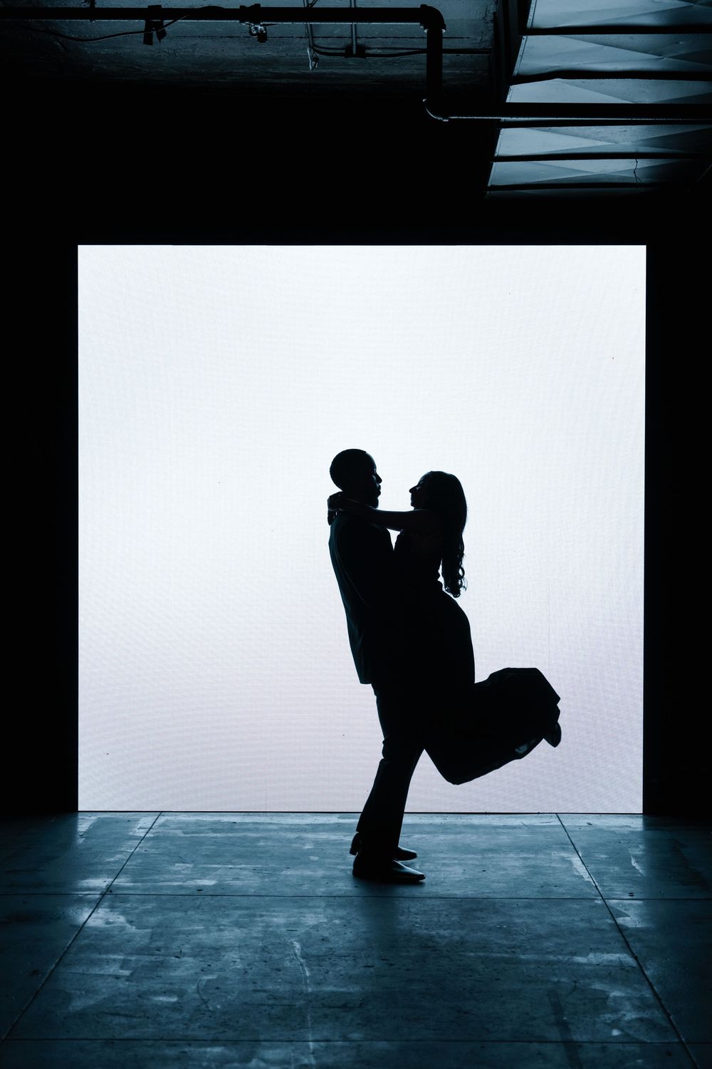 Silhouette of a romantic couple embracing in a dramatic backlit doorway with one person lifting the other.