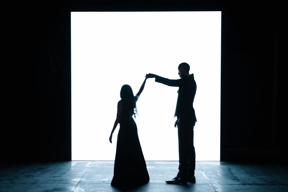 Silhouettes of two people dancing together in dramatic lighting against a dark background.