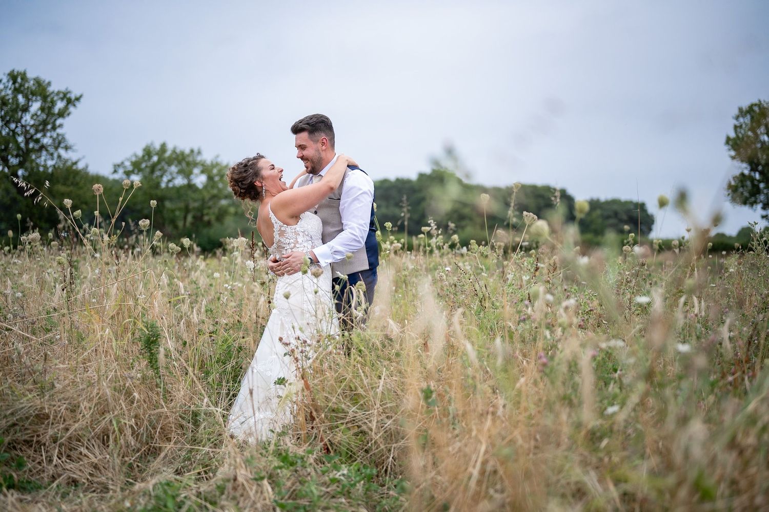 A couple shares an intimate moment together in a sunlit meadow filled with tall grass and wildflowers.
