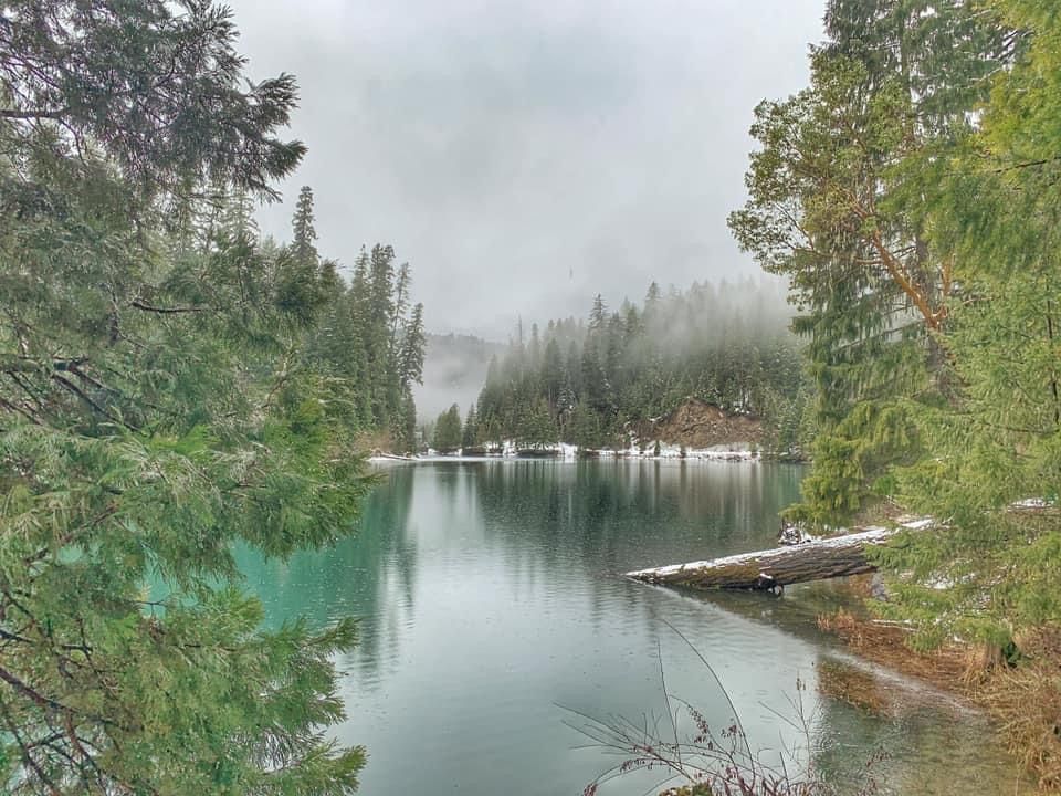 Misty lake with turquoise waters surrounded by evergreen trees and a wooden dock in the Pacific Northwest wilderness.