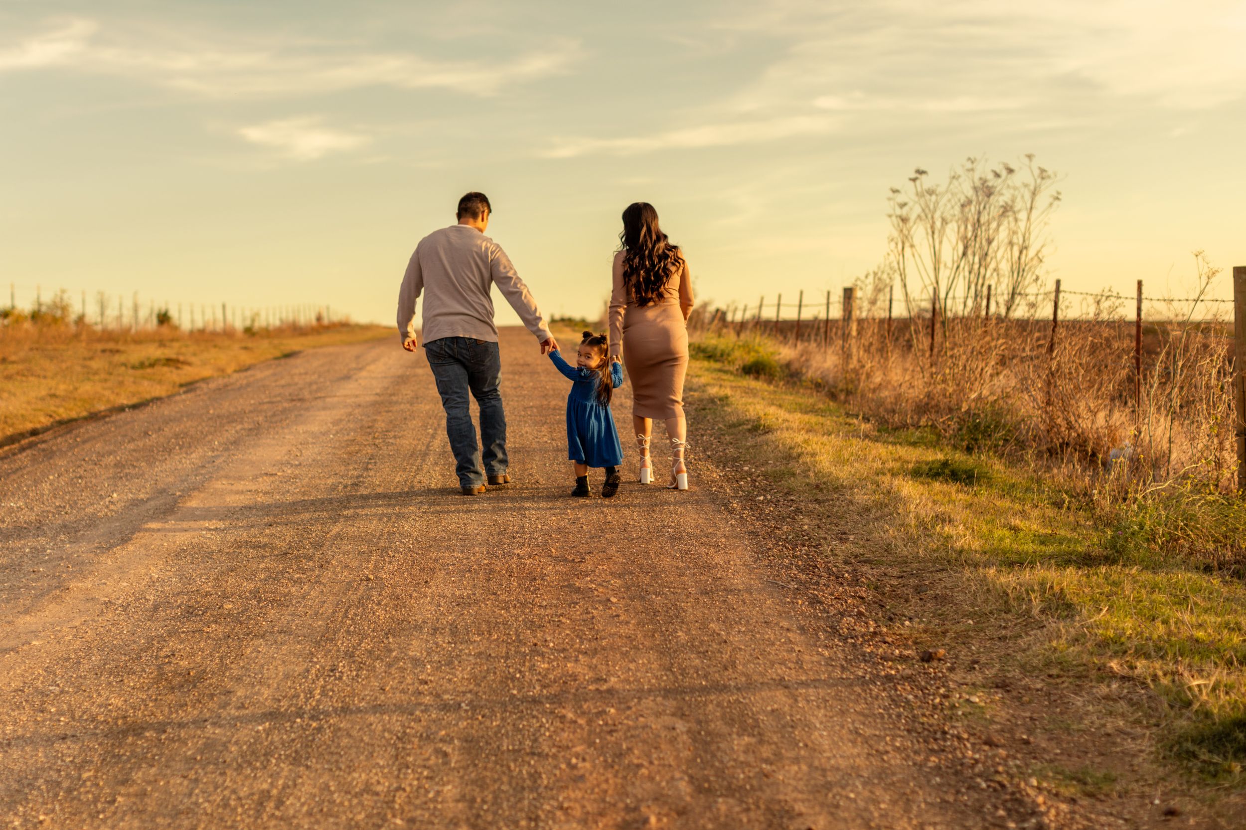 A family walks together holding hands on a dirt road during golden hour.