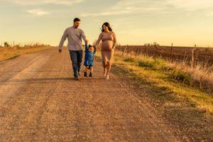 A couple holds hands with their child while walking on a rural road during sunset.