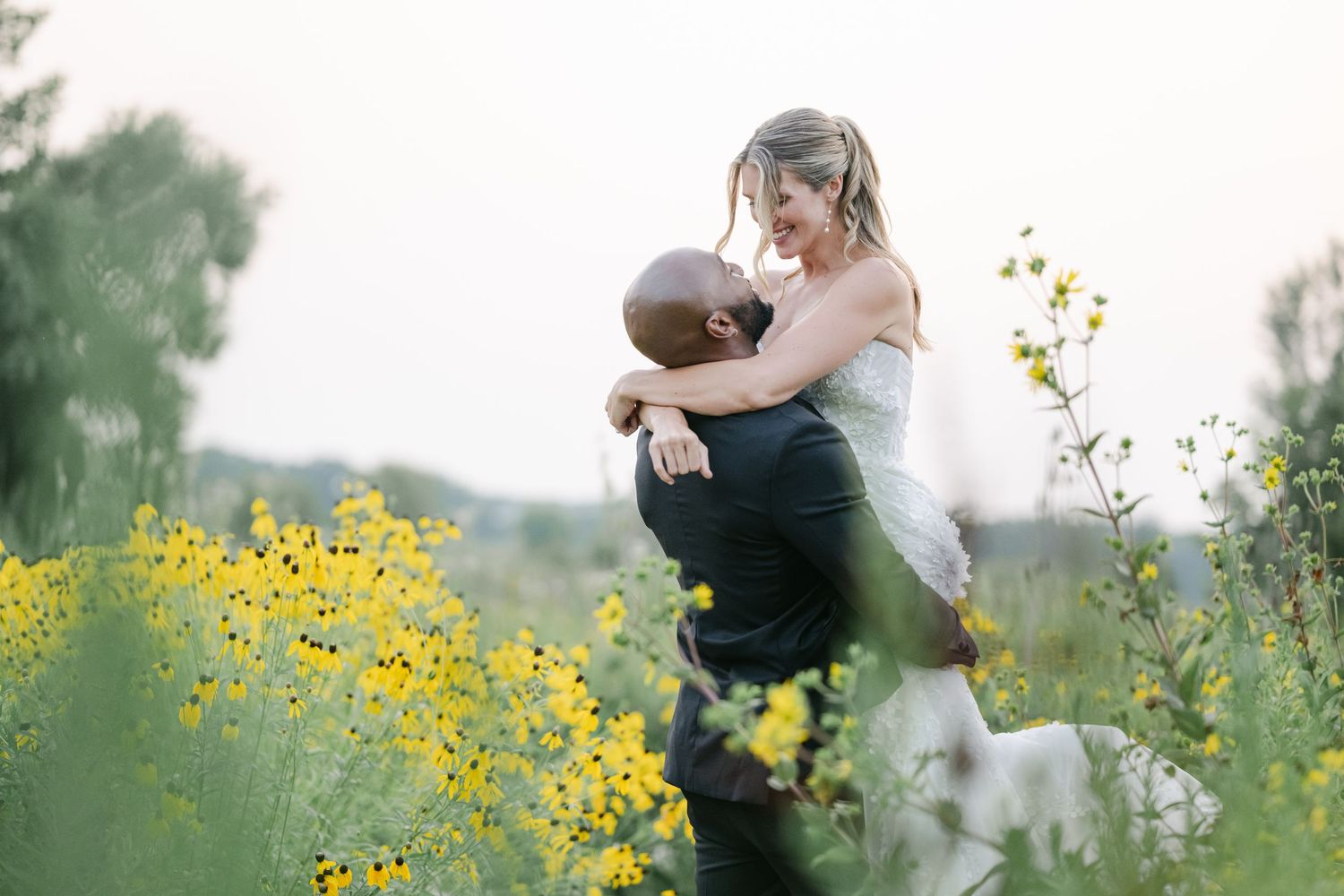 A couple embraces in a golden field of wildflowers during sunset creating a romantic silhouette. - Elawa Farm