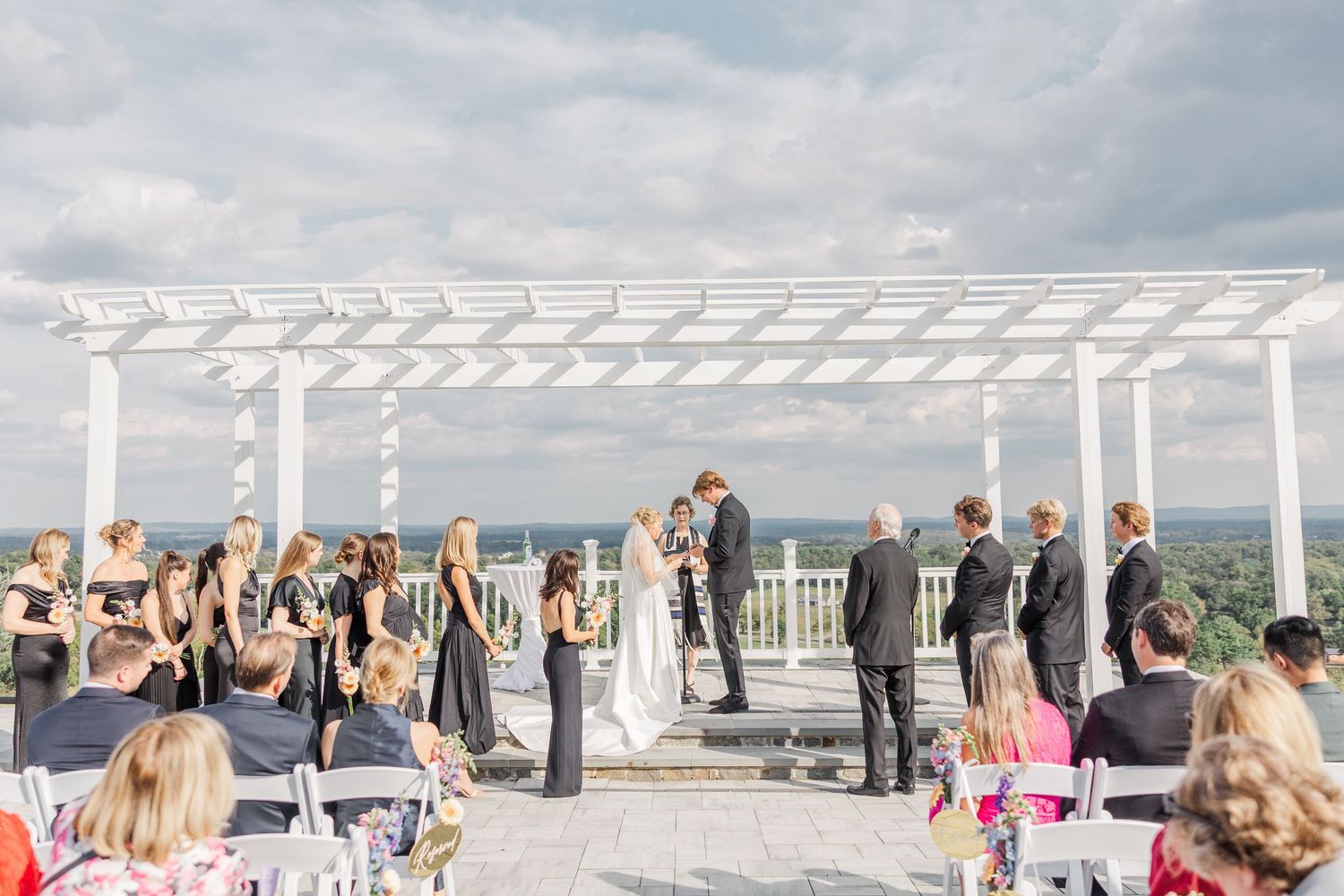 Outdoor wedding ceremony setup with white pergola and guest seating overlooking a scenic mountain landscape.