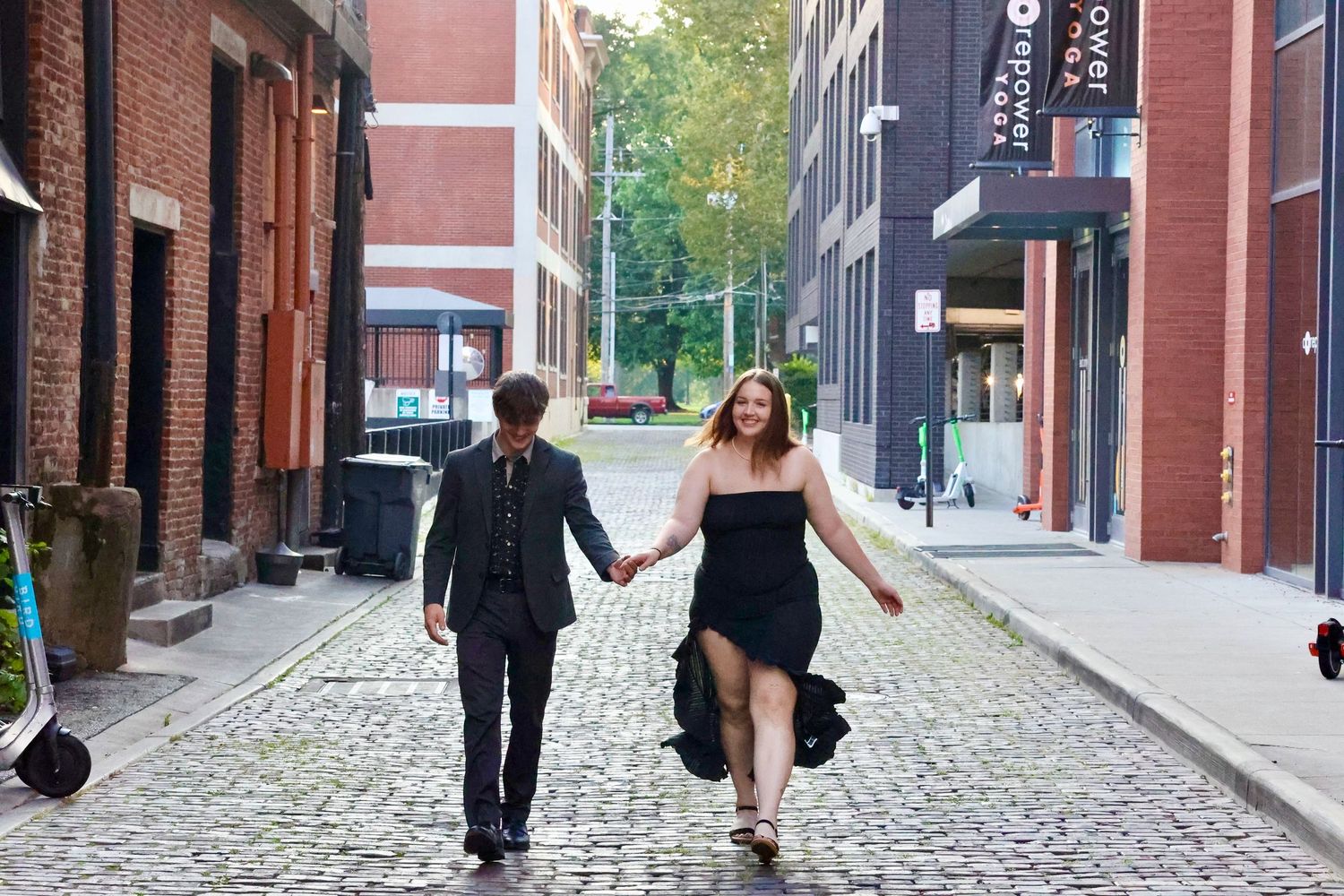A couple walks hand in hand down a cobblestone street between brick buildings.