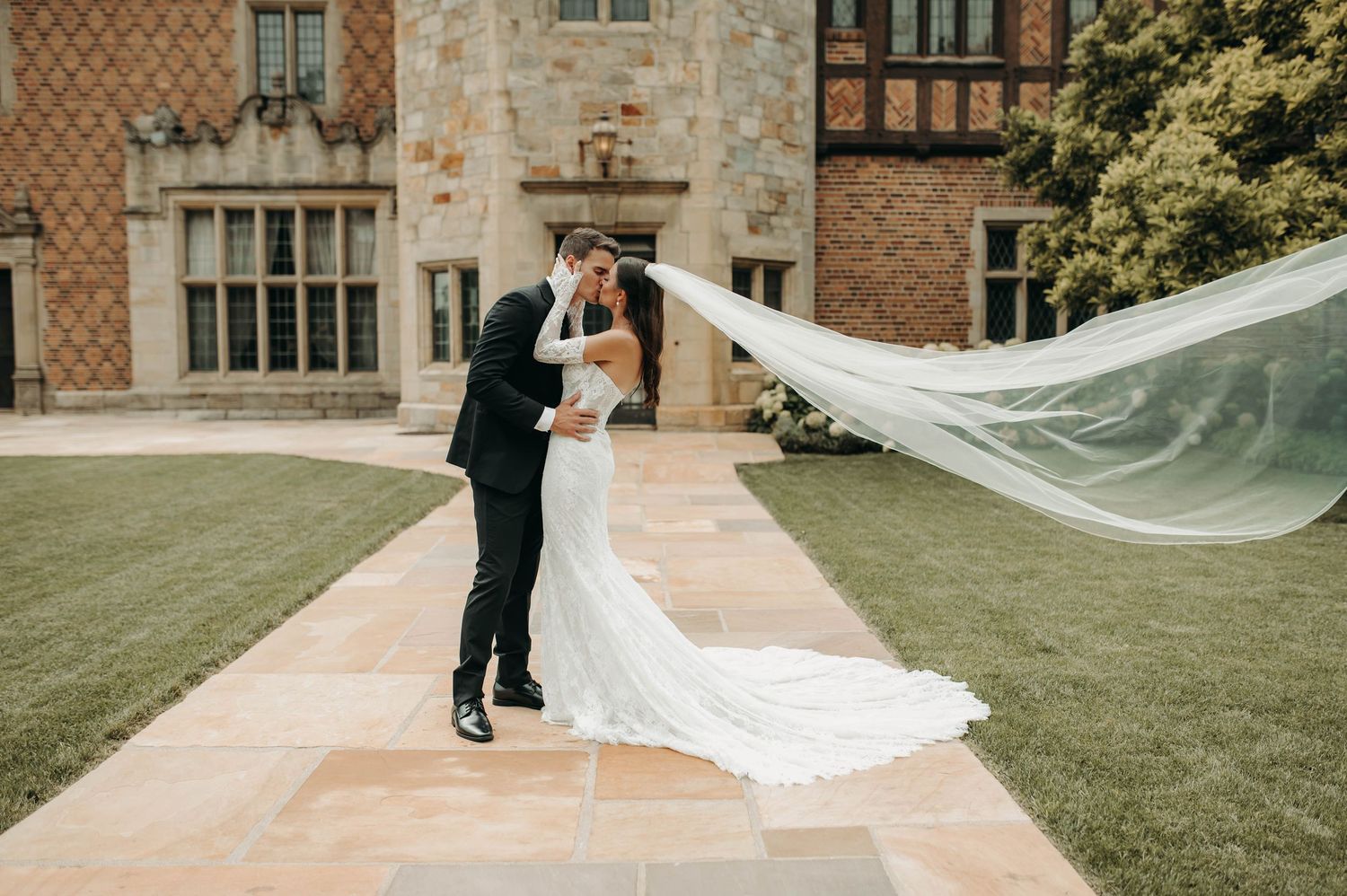 Bride and groom kissing with flowing veil at a grand estate wedding venue.