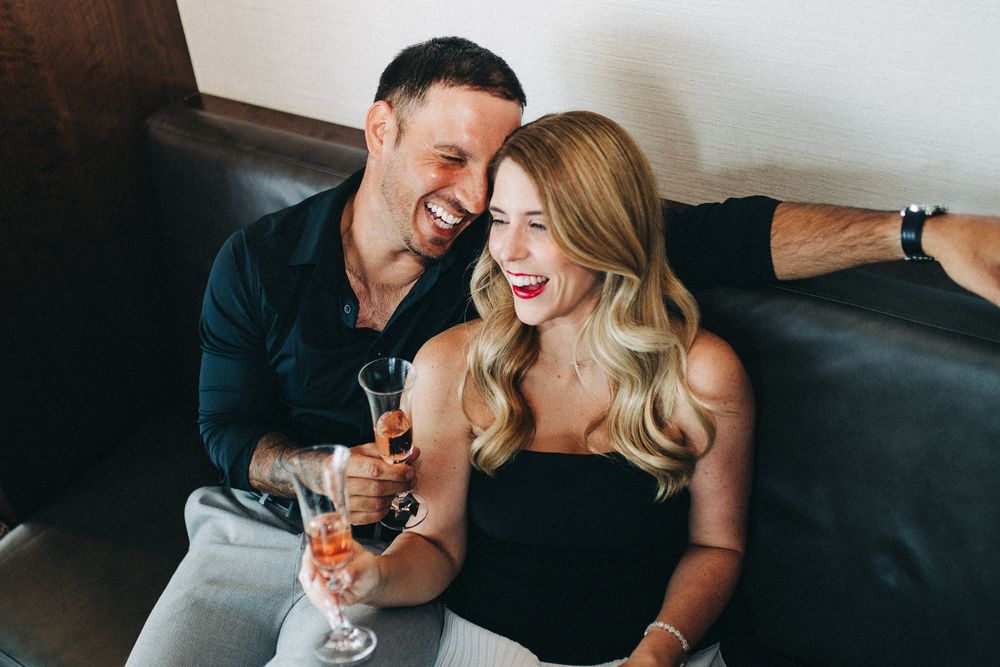 A romantic moment between a couple laughing and enjoying wine on a dark sofa.