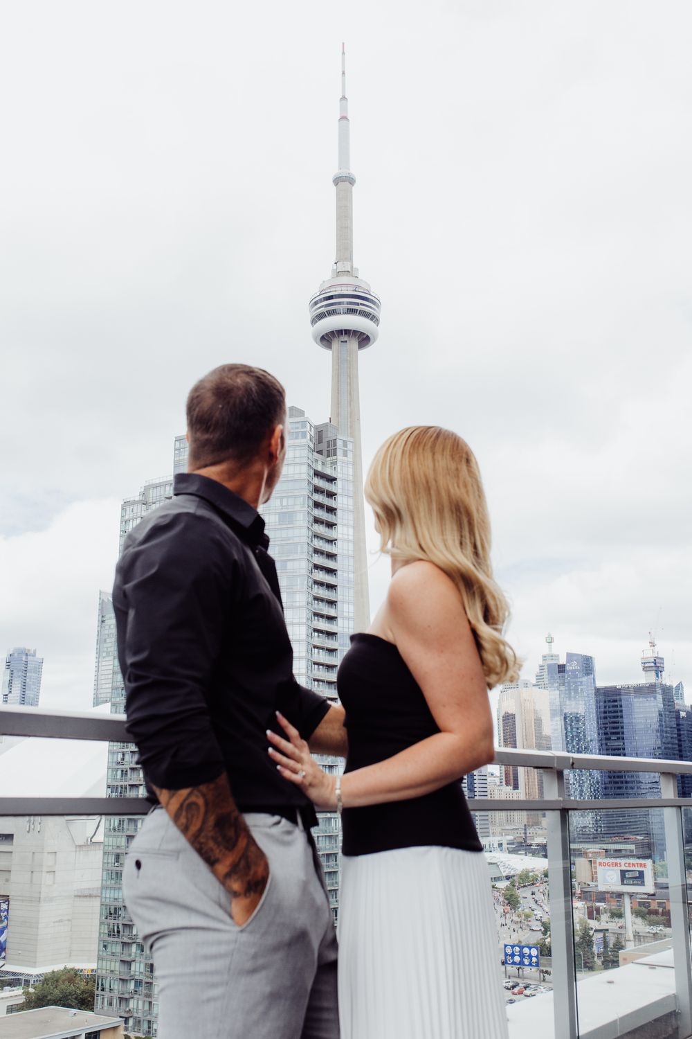 Couple sharing a romantic moment on a rooftop terrace with Toronto's CN Tower and skyline in the background.